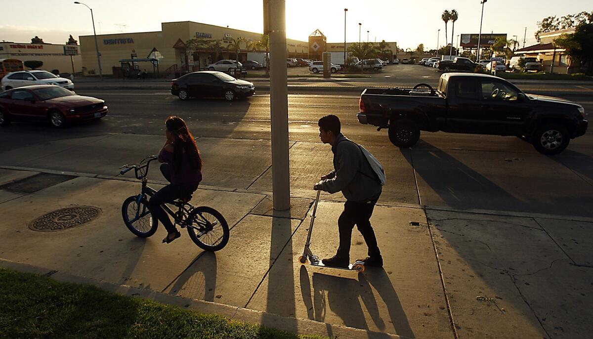 Kids scoot down Harbor Boulevard in Santa Ana as late afternoon traffic rolls along a landscape of strip malls. Despite real estate development, the boulevard has seen little change over the years. There is no equivalent of the light-rail expansion that is remaking L.A., neither is there a large infusion of bike lanes or a rethinking of pedestrian access that would better engage with the landscape.