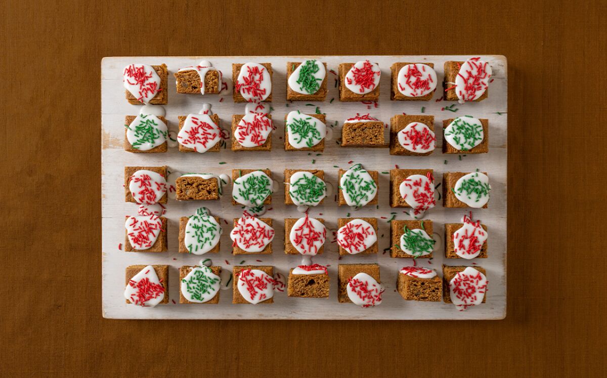 Cookies cut into squares and topped with white dollops of icing and red and green sprinkles.