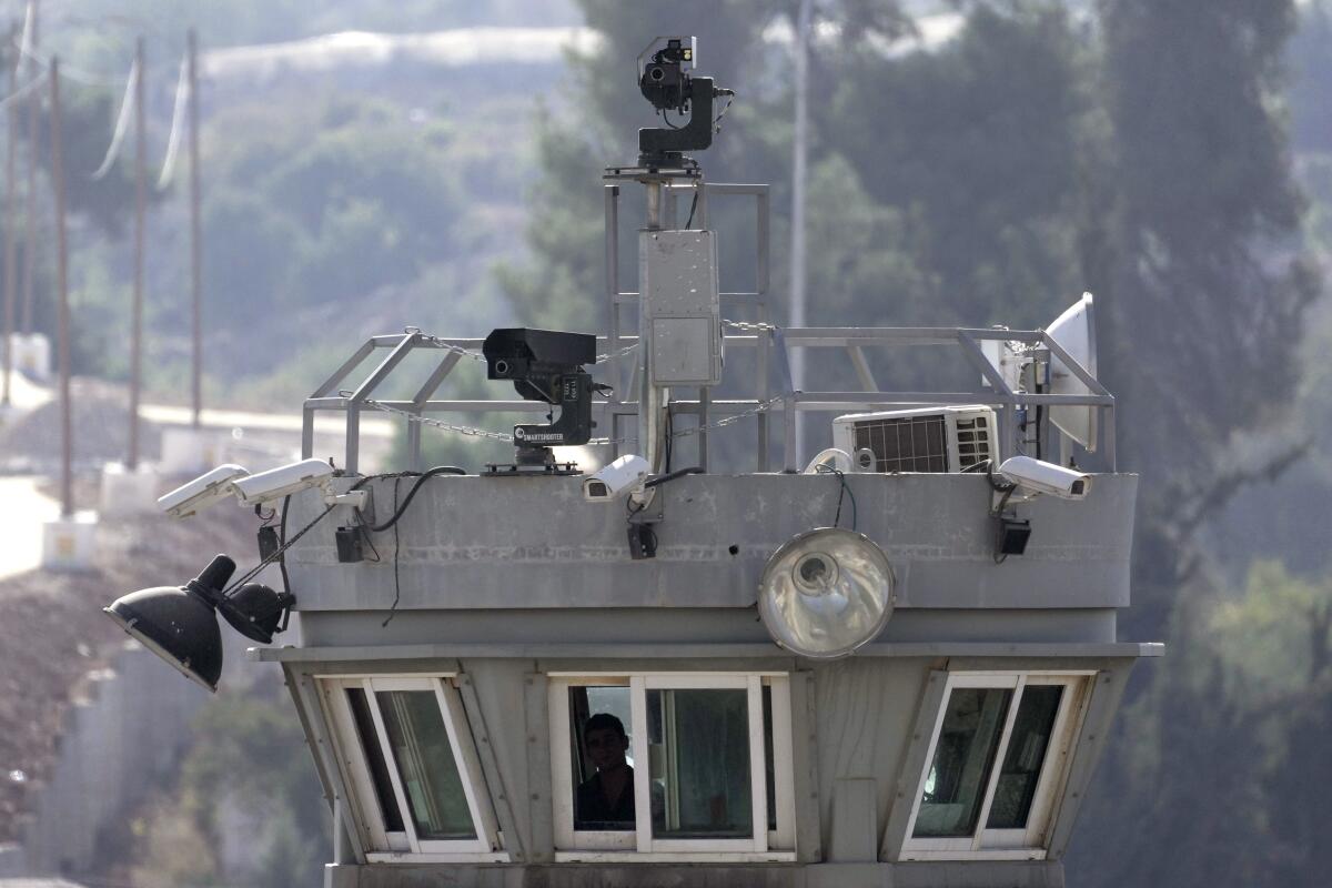 Two robotic guns sit atop a guard tower bristling with surveillance cameras.