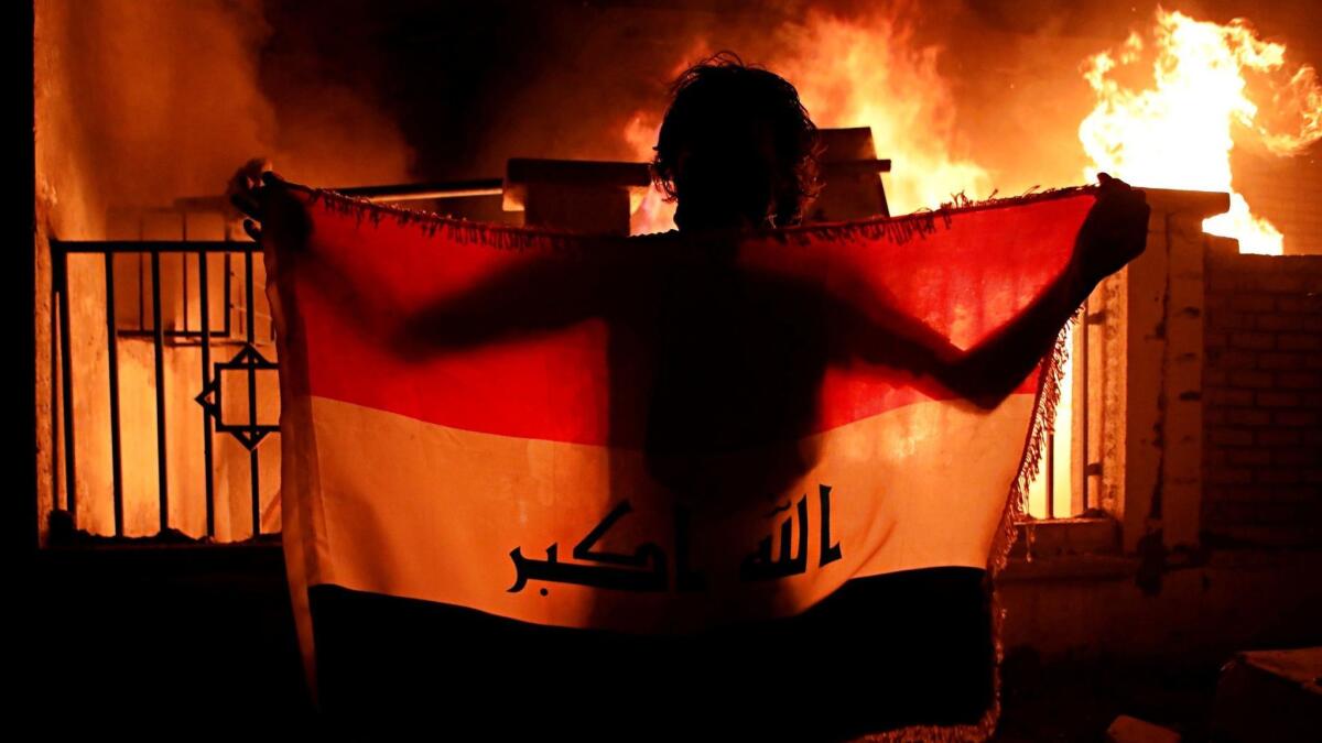 A man holds a national flag while protesters burn a municipal complex in Basra on Sept. 5.