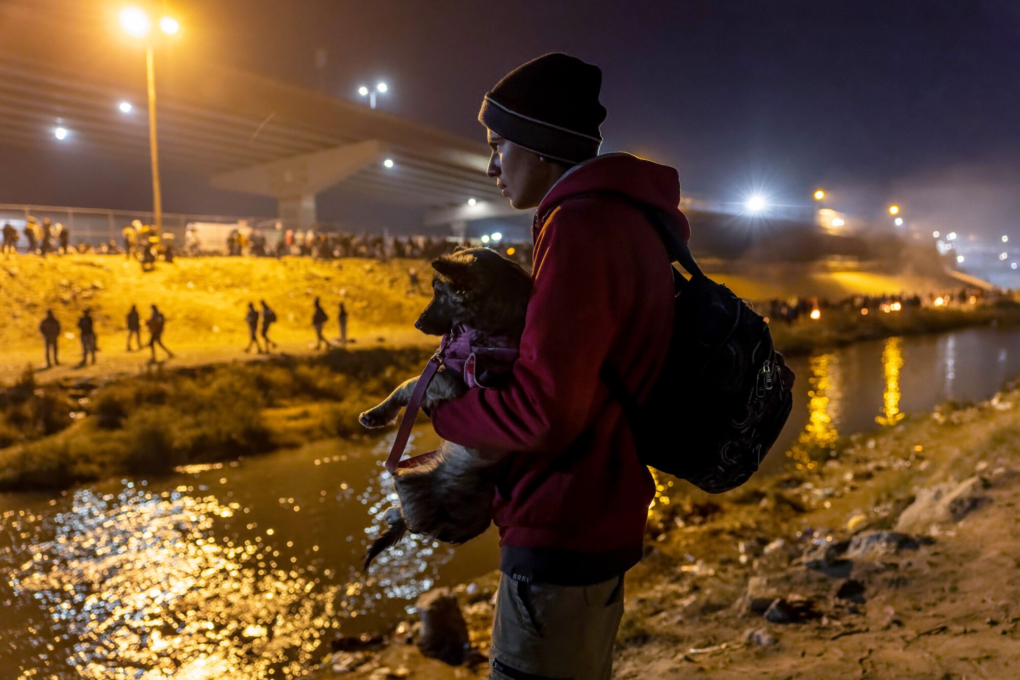 A migrant Jaider holds his puppy while looking over the Rio Grande into El Paso.