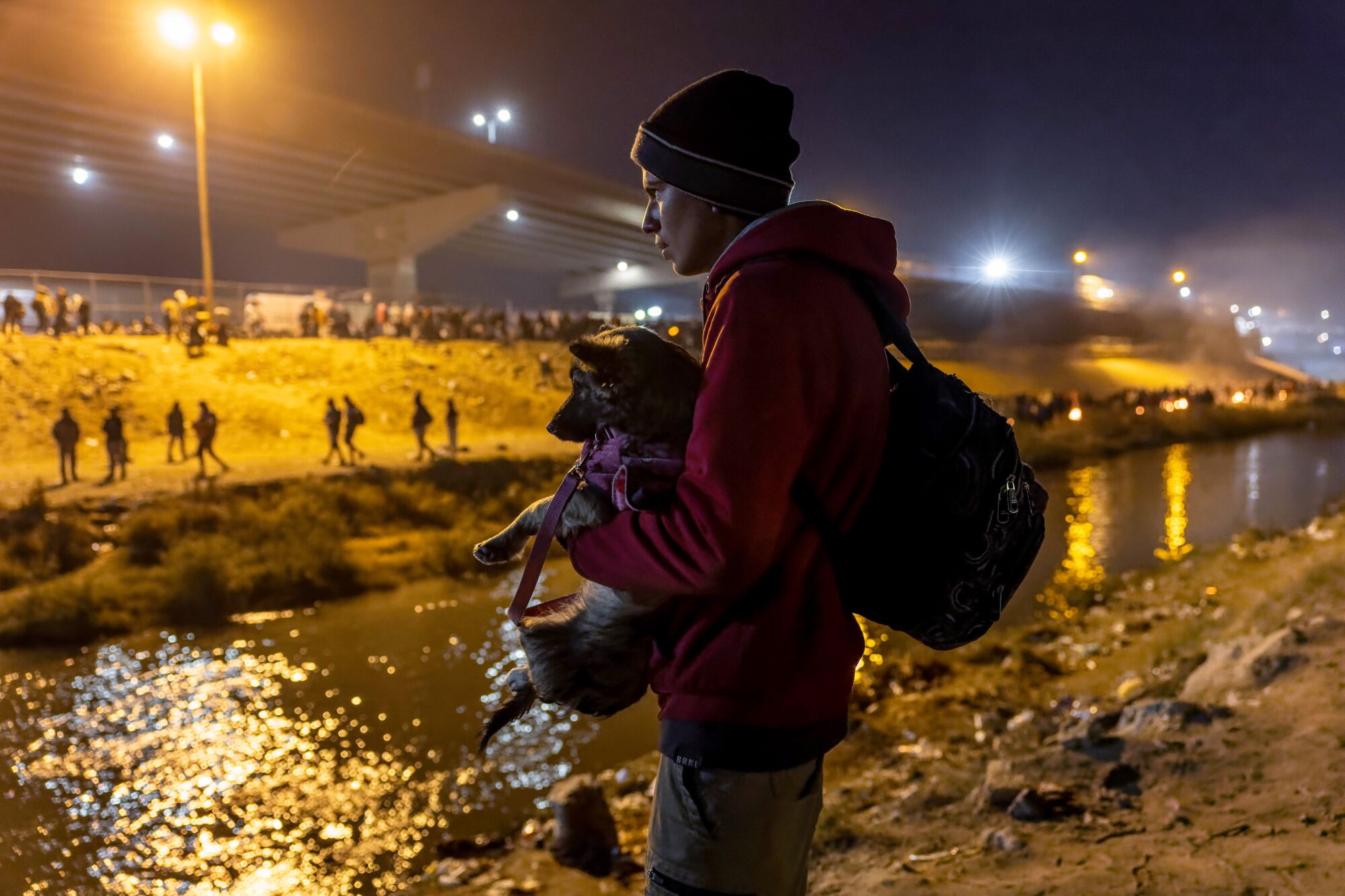 A boy holds a dog as he faces a river 