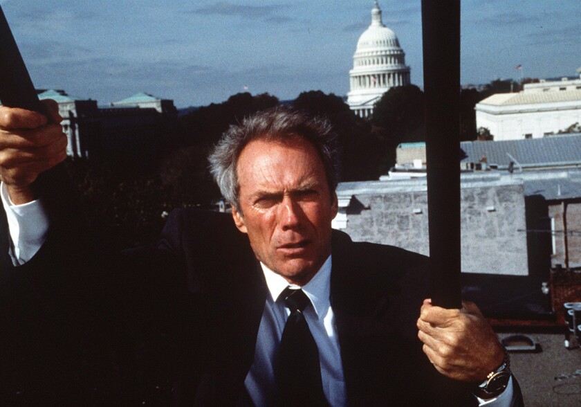 A man in a dark suit and tie hangs onto some bars in the film "In the Line of Fire."