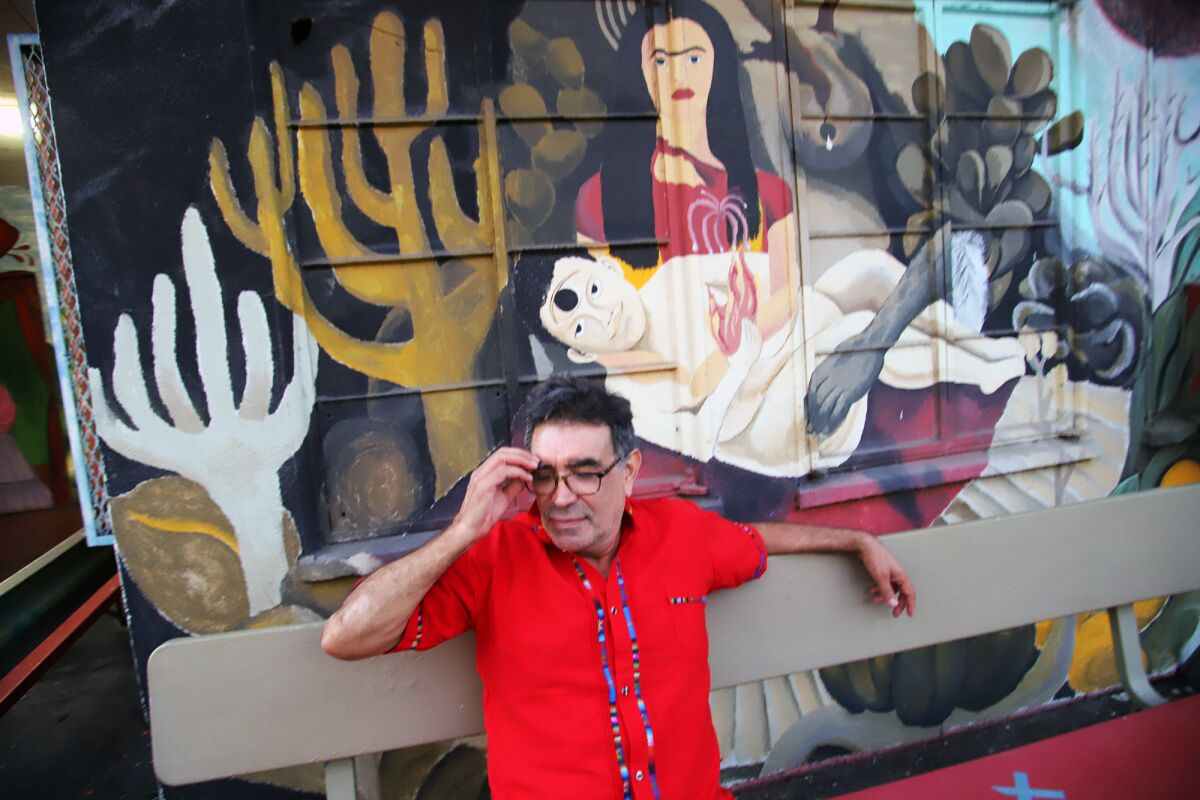 A man in a red shirt on a bench in front of a mural