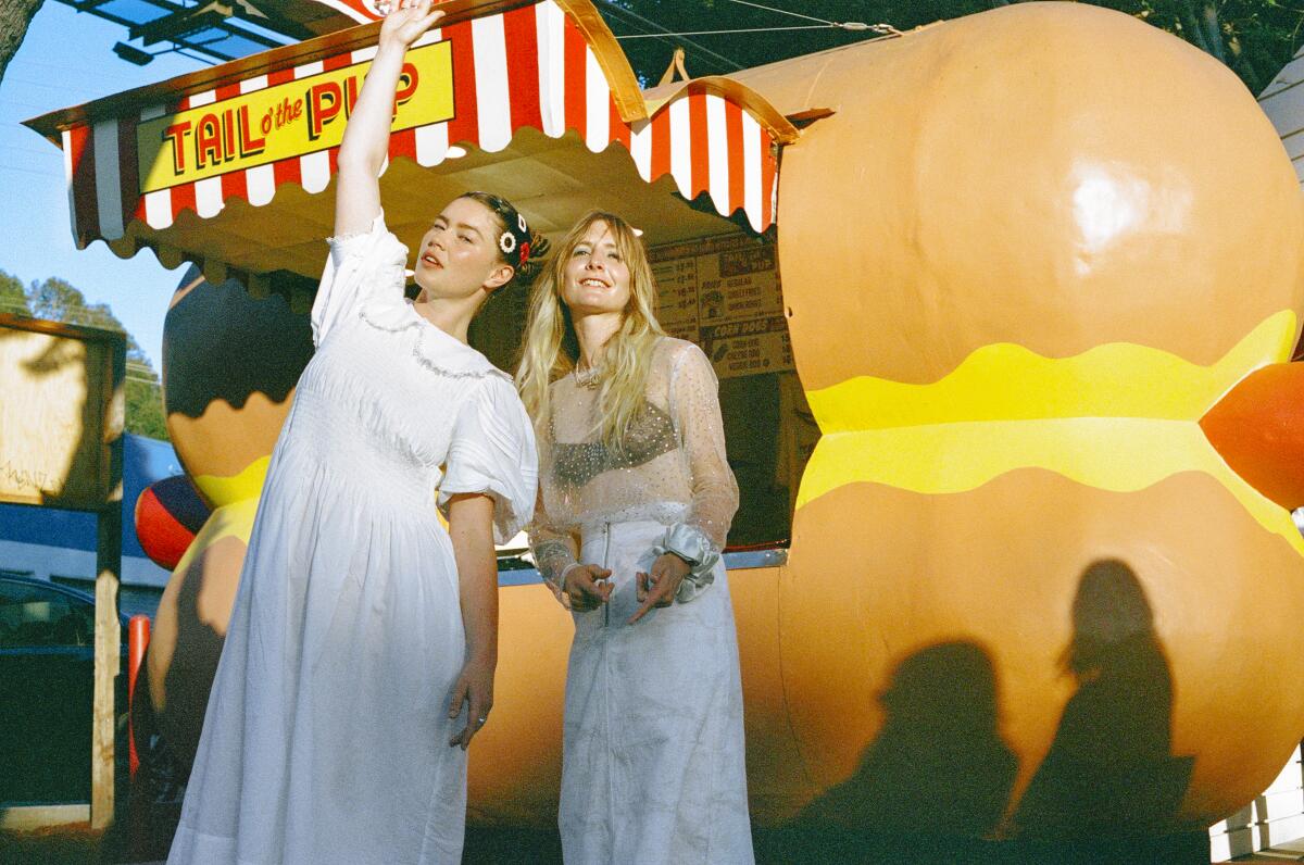 Two women stand in front of a hot dog stand.