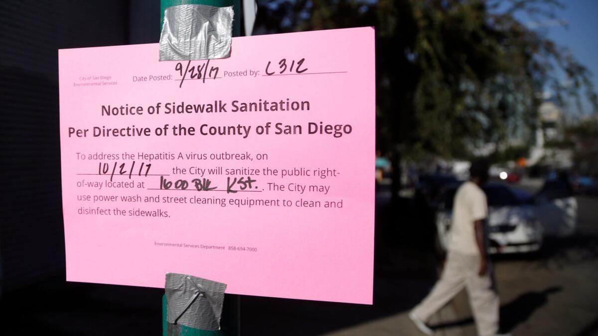 A man passes behind a sign warning of an upcoming street cleaning along 17th Street in San Diego.