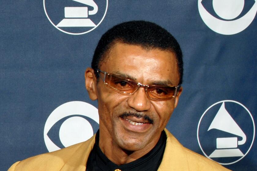 Ike Turner Jr. smiles in a yellow jacket and tinted rectangular glasses.