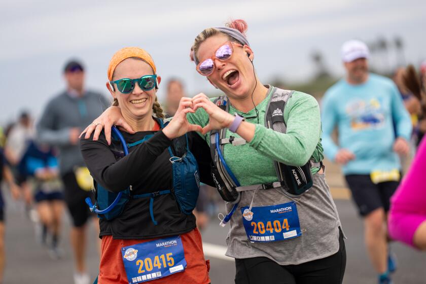 Catherine Barker and Becky Bravo, both of Costa Mesa, make a heart sign during Sunday morning's Surf City Marathon.