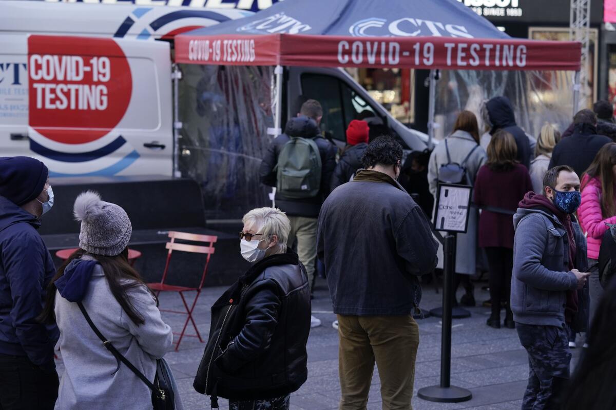 People in coats and hats and face masks stand outside a tent that says "COVID-19 Testing."