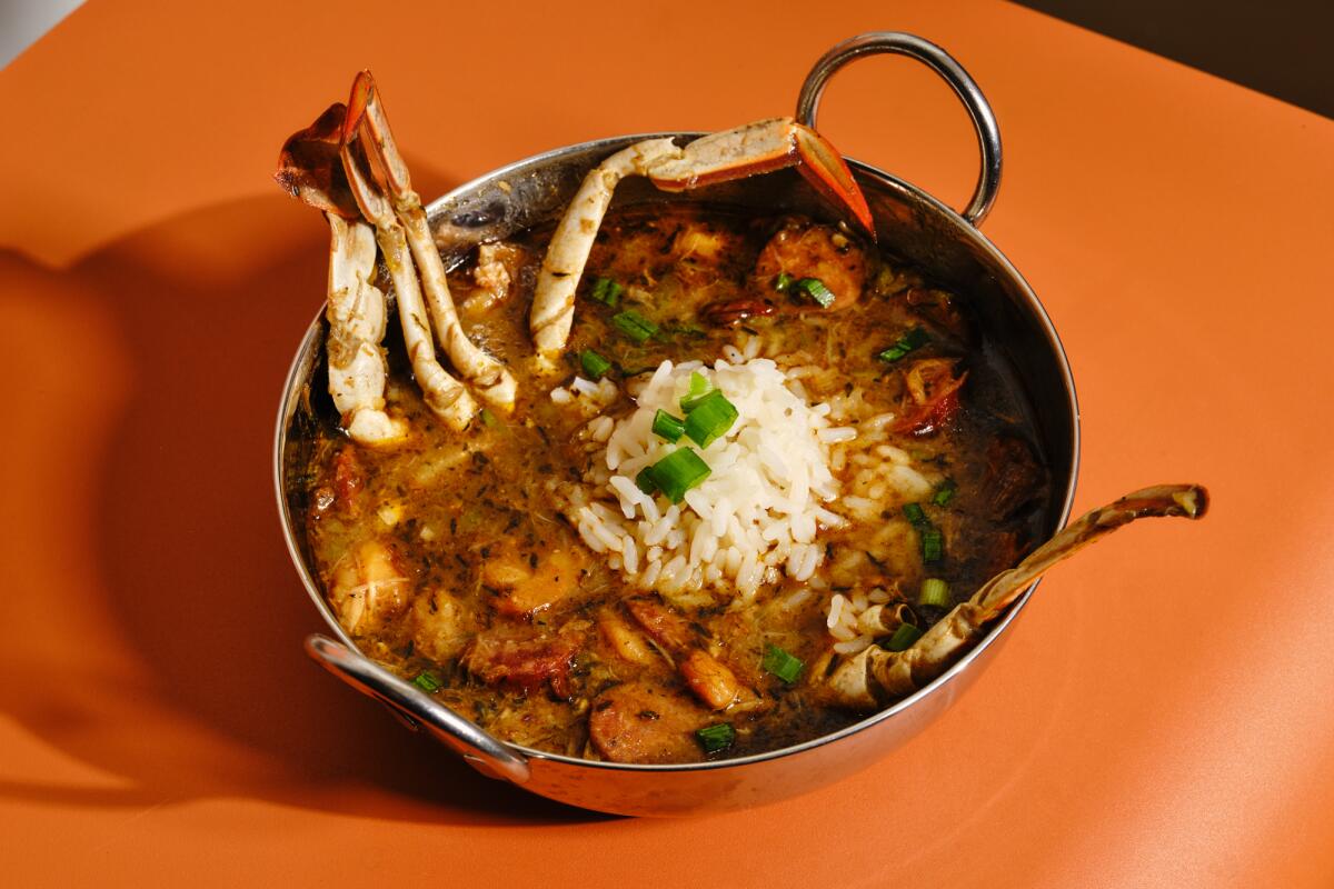 A metal bowl of gumbo with rice on an orange table 