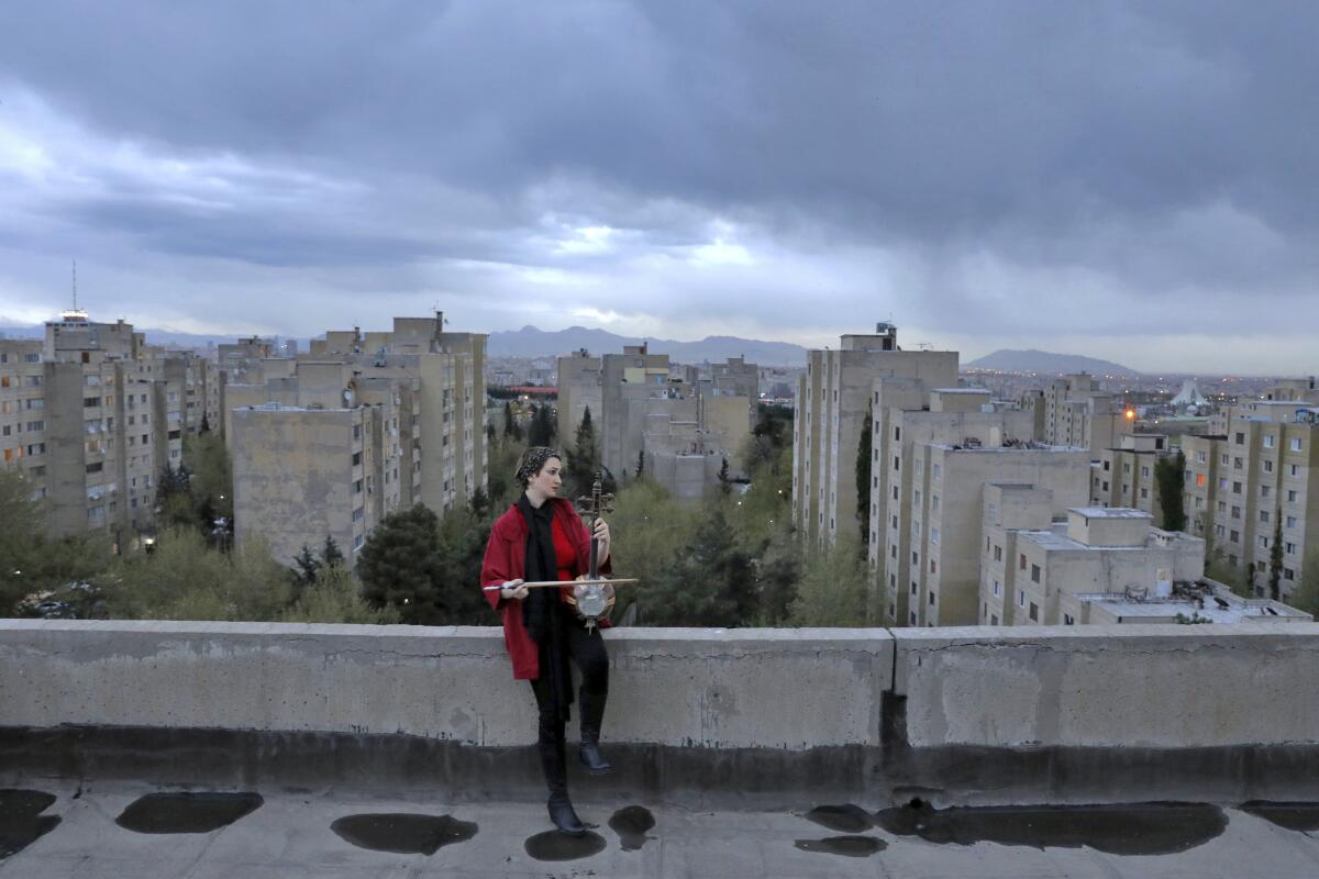 Fotografía del 20 de marzo de 2020 de la música Shiva Abedi, de 30 años, tocando el kamanchen en la azotea de su casa durante la cuarentena obligatoria debido al brote del nuevo coronavirus en Teherán, Irán. (AP Foto/Ebrahim Noroozi)