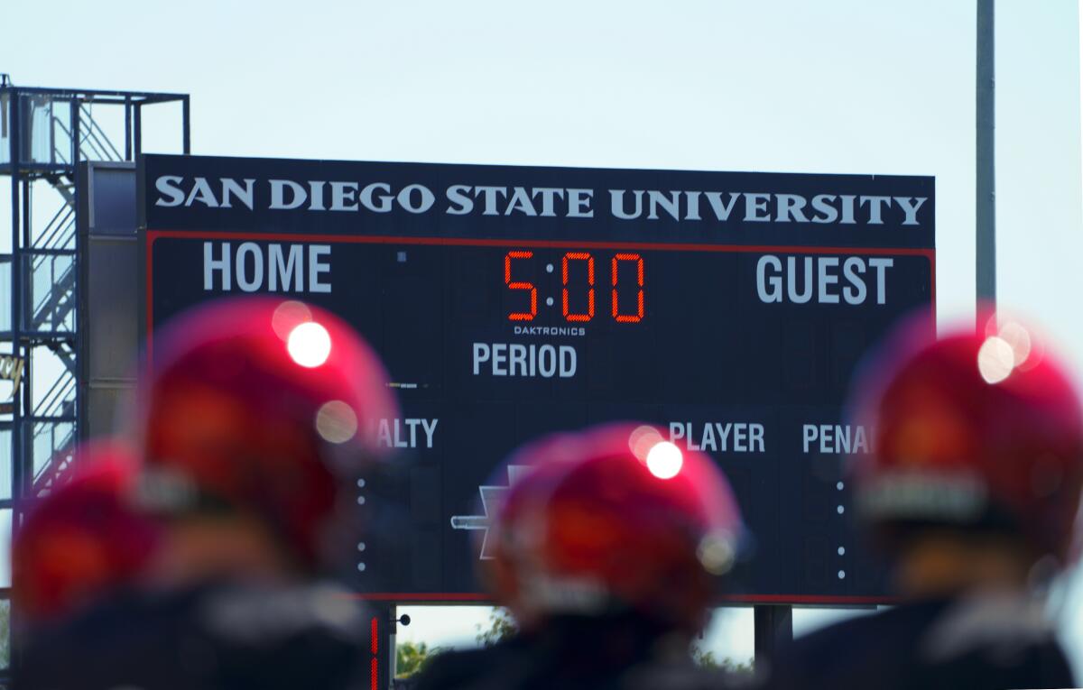 Helmeted players stand in front of a scoreboard that bears the San Diego State University name.