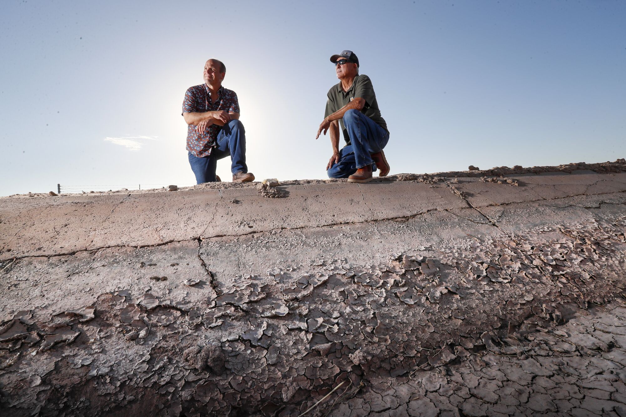 Imperial Valley farmers Jack Vessey, left, and Danny Robinson kneel by the edge of an irrigation ditch.