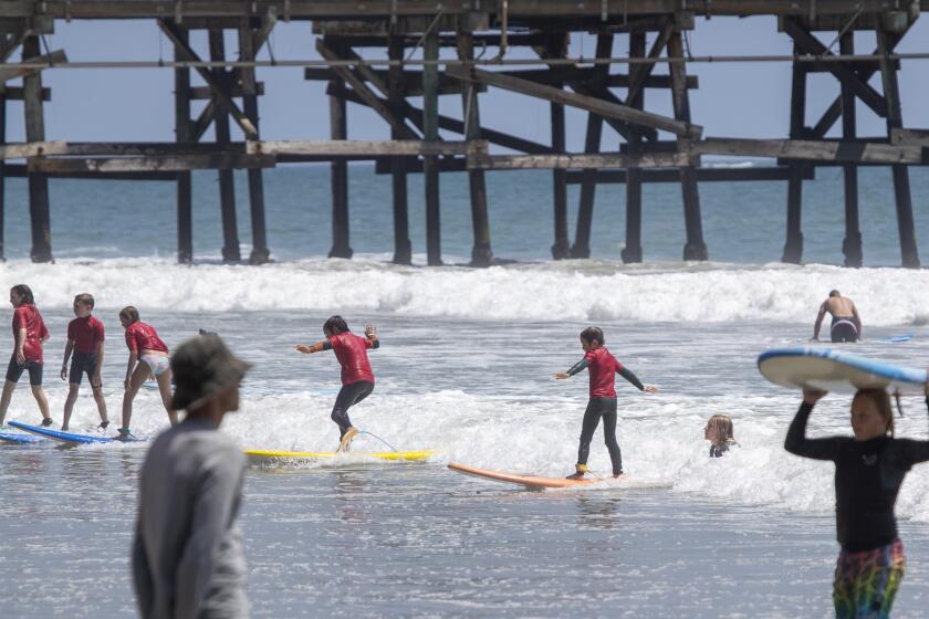 SAN CLEMENTE, CA - JUNE 30: Kids ride a wave together as they learn to surf on a warm summer day at the San Clemente Pier Tuesday, June 30, 2020. Heal the Bay released its annual Beach Report Card and the San Clemente Pier made the top 10 list of beach bummers. (Allen J. Schaben / Los Angeles Times)