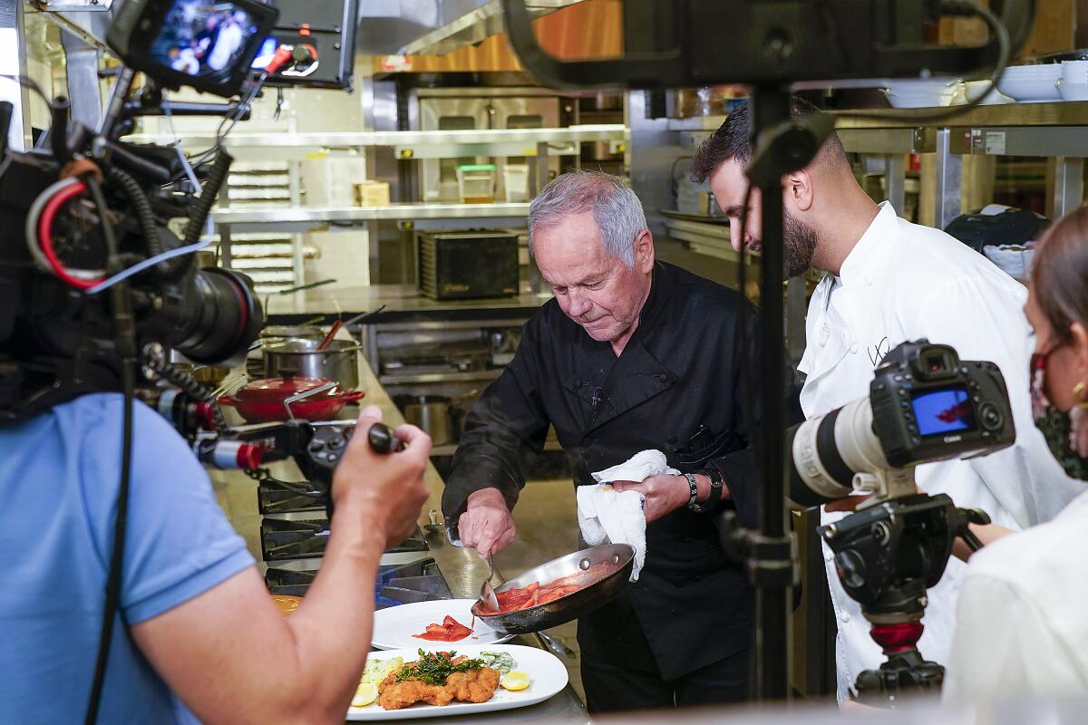 Wolfgang Puck plates a dish of food as director David Gelb and a camera crew watch.