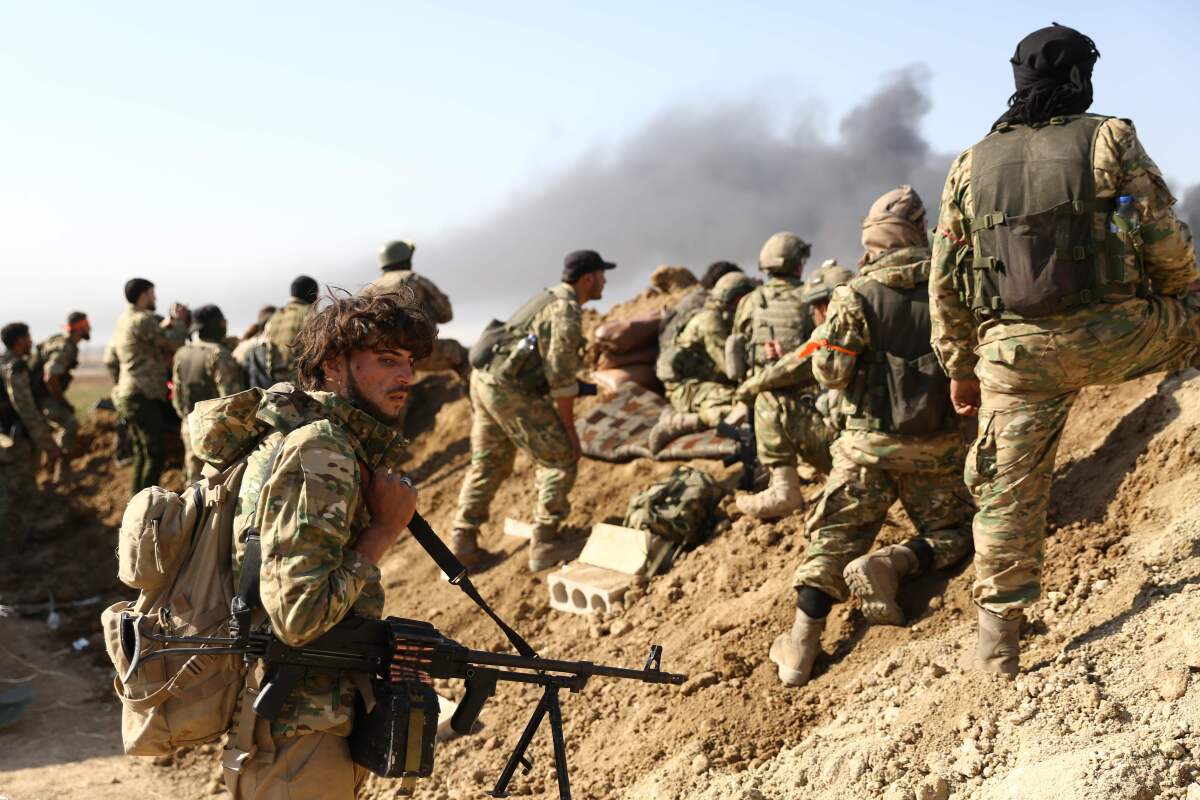 Soldiers watch as smoke billows from the border town of Ras al-Ayn, Syria.