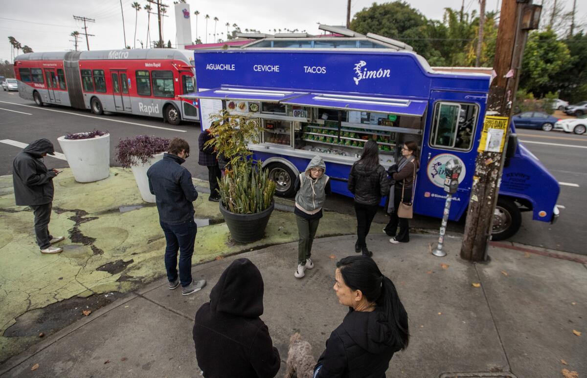 Customers wait for their orders at the Simon mariscos truck parked at the Sunset Triangle Plaza.