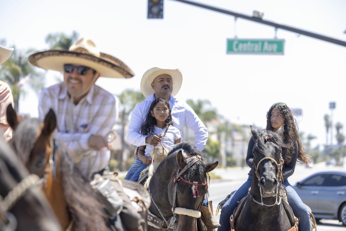 Men and children ride horses on a city street.