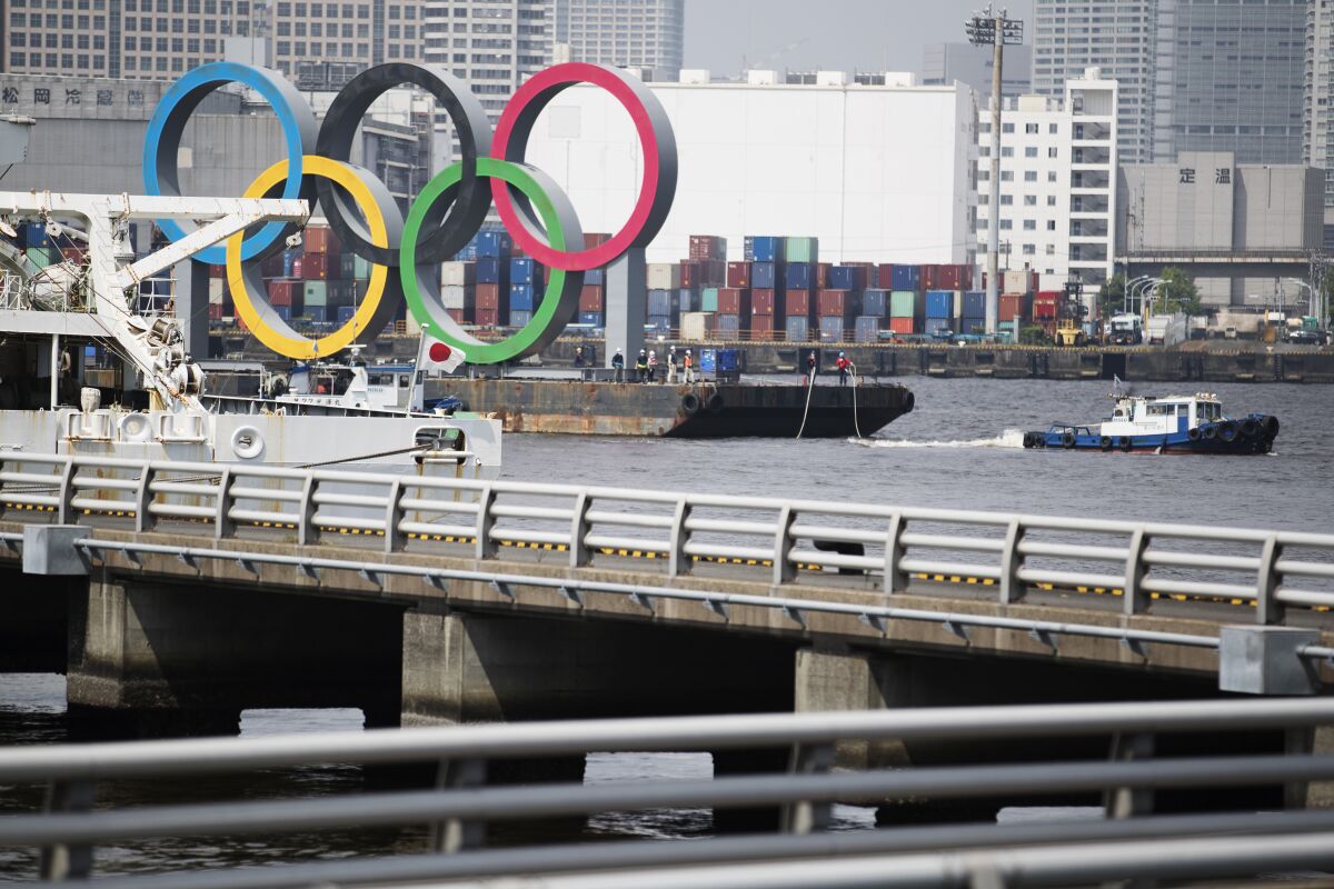 Tugboats move a symbol installed for the Olympic and Paralympic Games Tokyo 2020 on a barge from its usual spot off the Odaiba Marine Park in Tokyo Thursday, Aug. 6, 2020. The five Olympic rings floating on a barge in Tokyo Bay were removed on Thursday for what is being called “maintenance,” and officials says they will return to greet next year's Games. The Tokyo Olympics have been postponed for a year because of the coronavirus pandemic and are to open on July 23, 2021. The Paralympics follow on Aug. 24. (AP Photo/Hiro Komae)