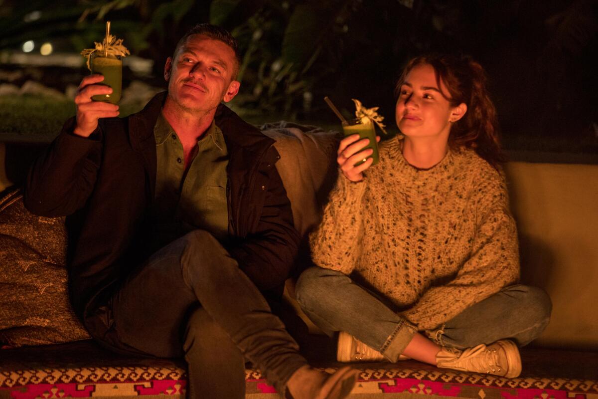 Two people hold up smoothies by a fire pit
