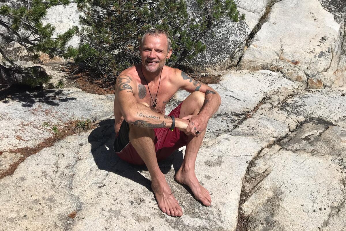 Flea poses for a photo in swim trunks, seated on a rock.