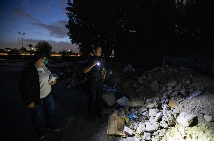 Amanda Hood and Officer Adam Hunter with the Fountain Valley Police Department stand next to a pile of rubble. 
