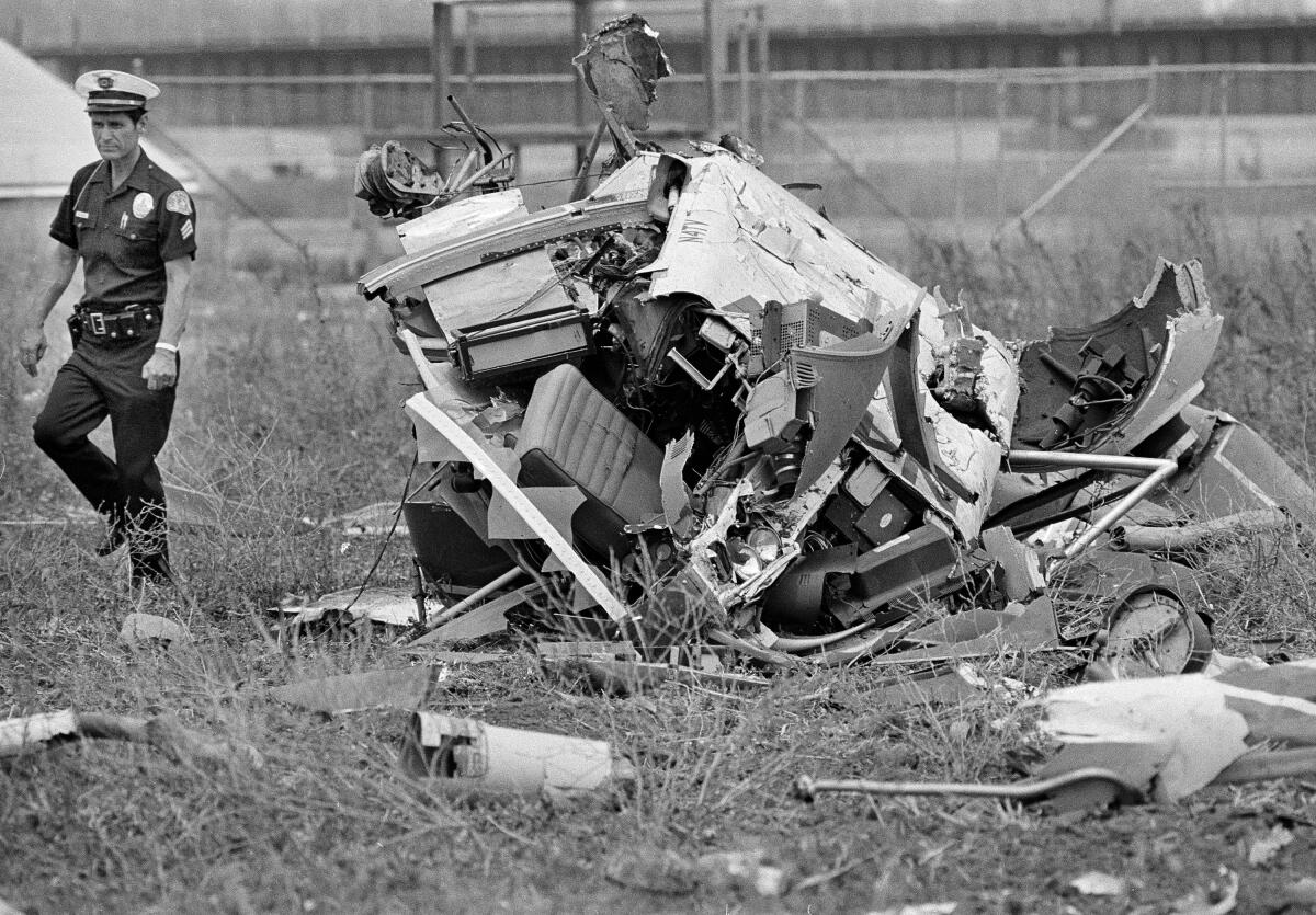 A man in a law enforcement uniform walks away from some mechanical wreckage.