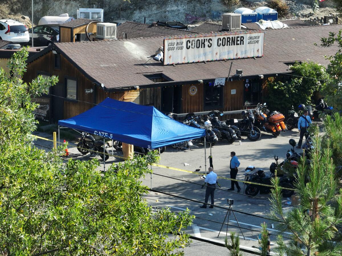 An aerial view of investigators next to a canopy and crime scene tape outside a bar with motorcycles parked outside