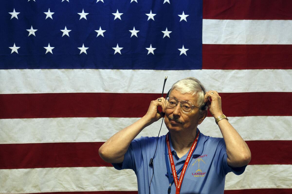 Pete Theisinger adjusts his headset, standing in front of an American flag, at the Jet Propulsion Laboratory