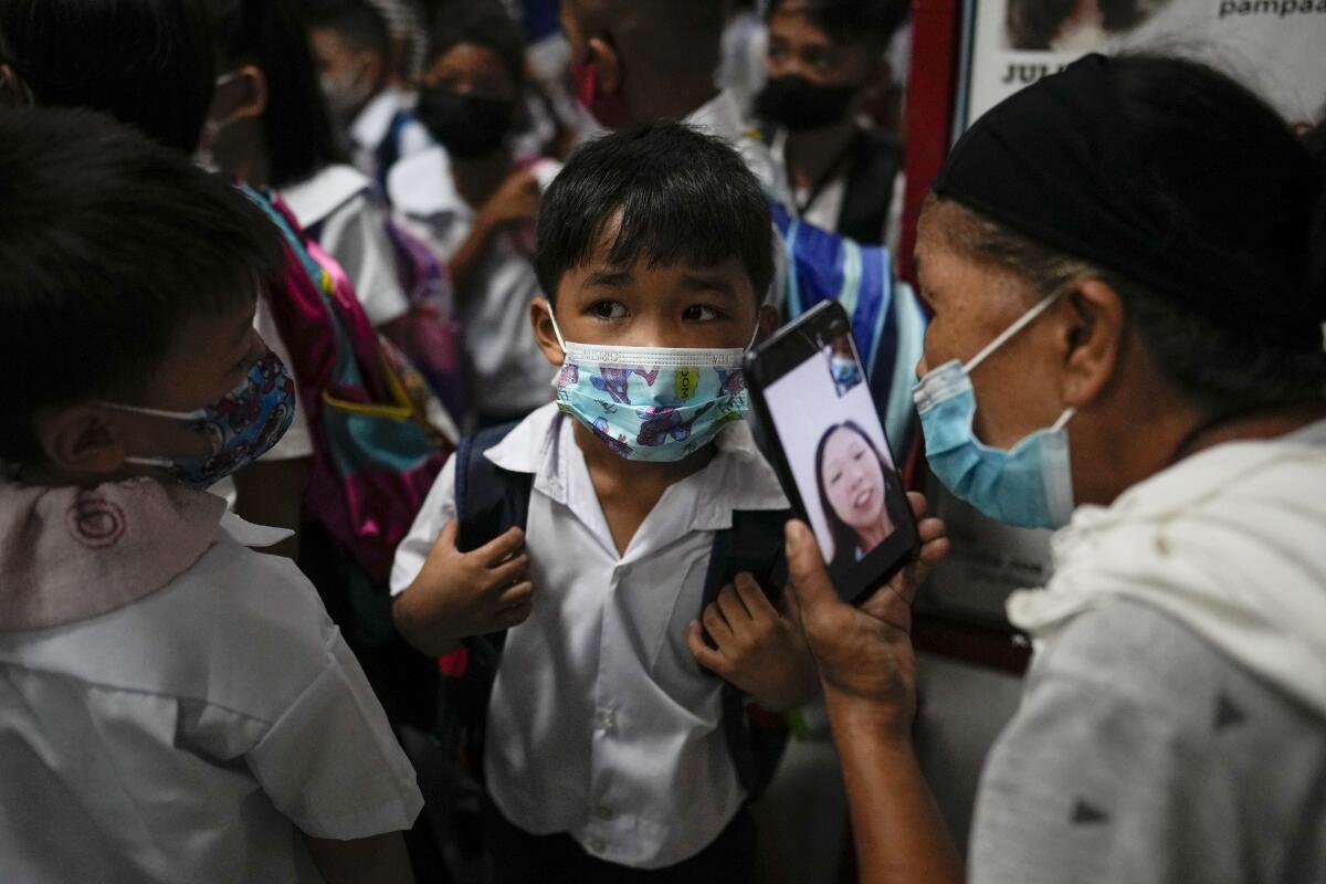 A boy talks to his mother on a cellphone while classmates stand near him.