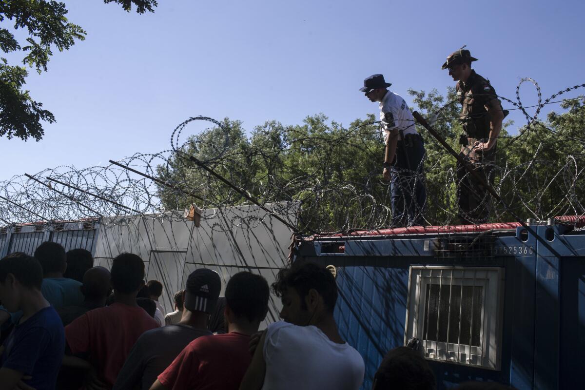 Policías y militares húngaros supervisan el reparto de comida mientras la gente hace fila en un campo migrante en la frontera serbia con Hungría, en Horgos, Serbia, el lunes 11 de julio de 2016. (AP Foto/Marko Drobnjakovic)