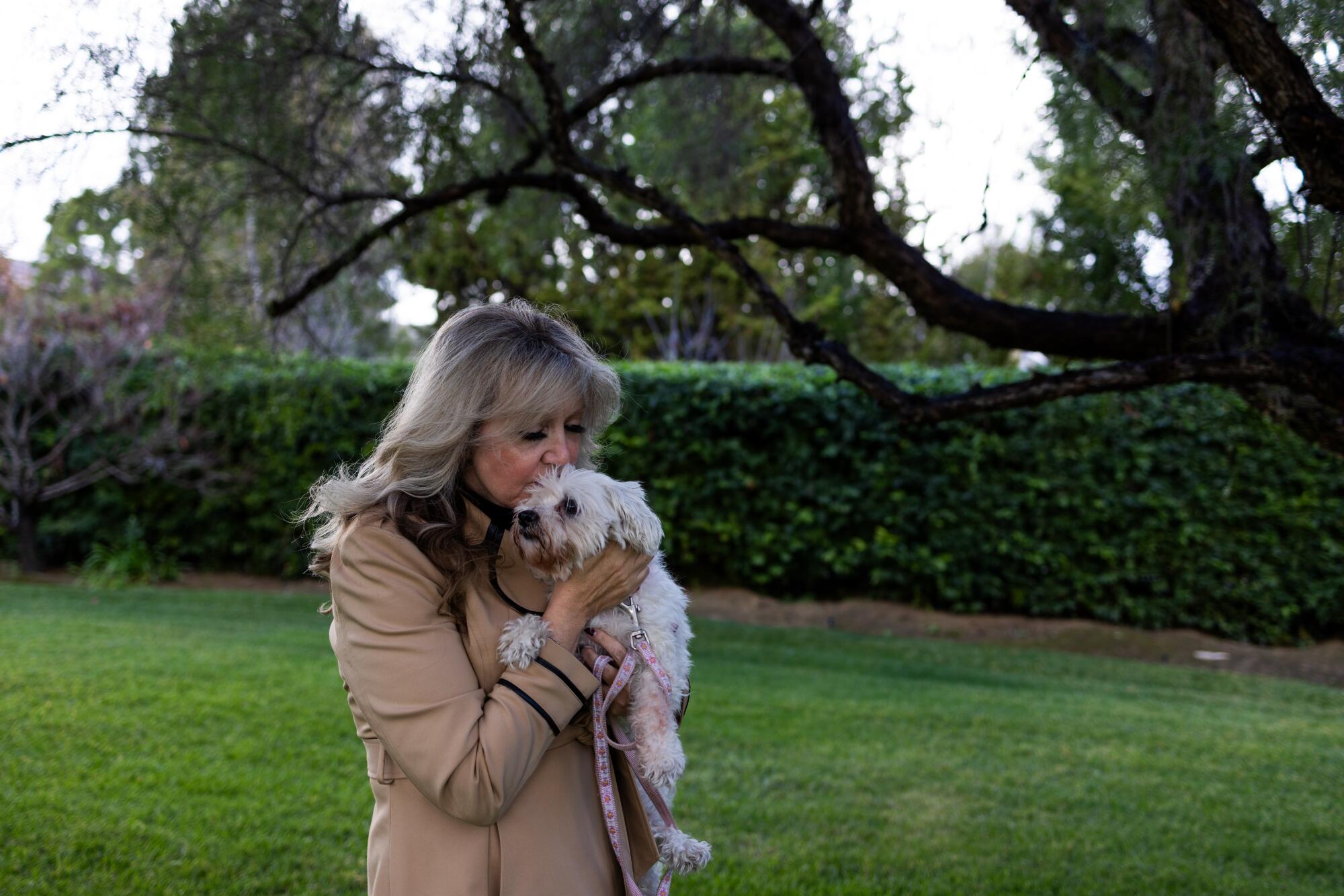 Holly Pinedo holding her Maltipoo Lacey in a grassy area with trees and a hedge