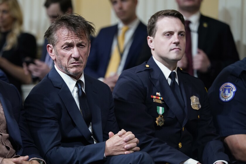 Sean Penn and an officer in police uniform listen.