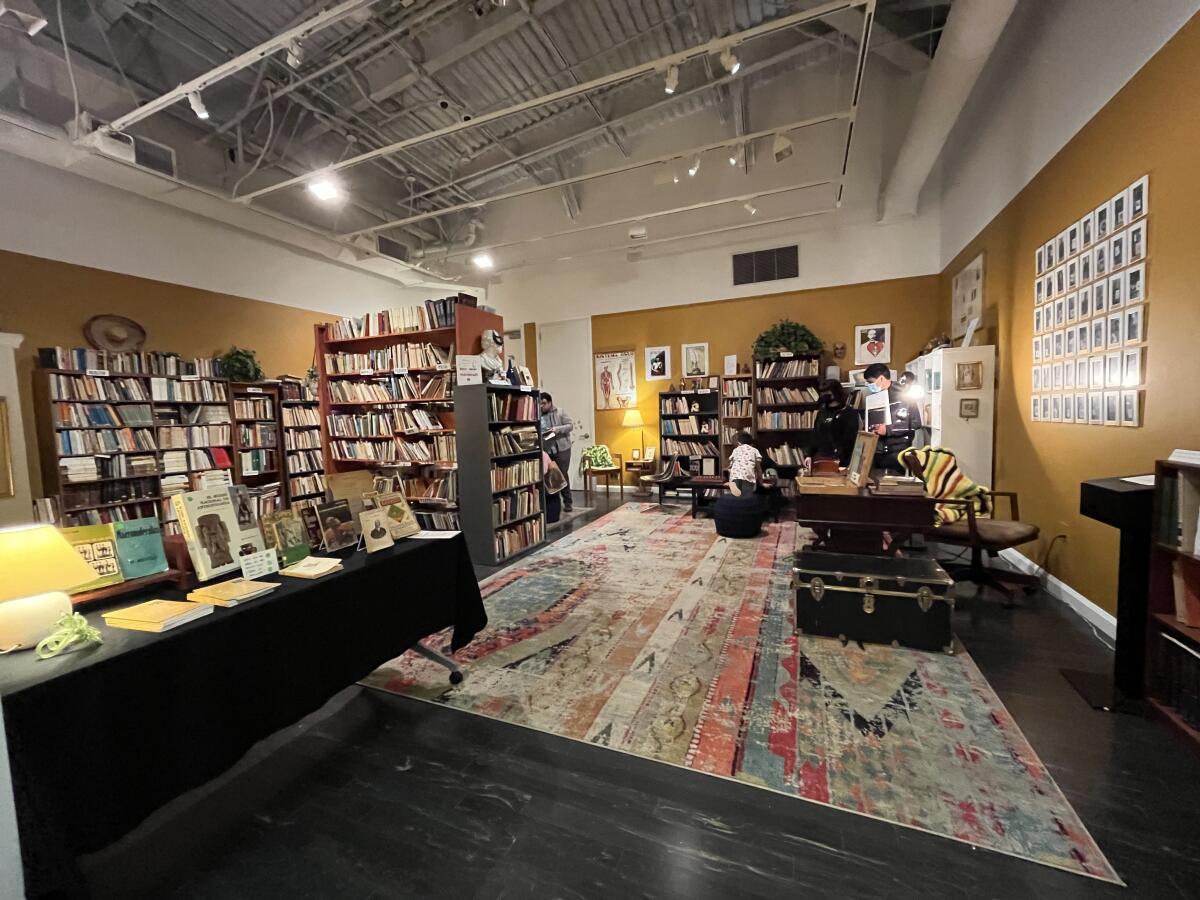 A museum gallery is transformed into a cluttered bookshop with mustard-colored walls.