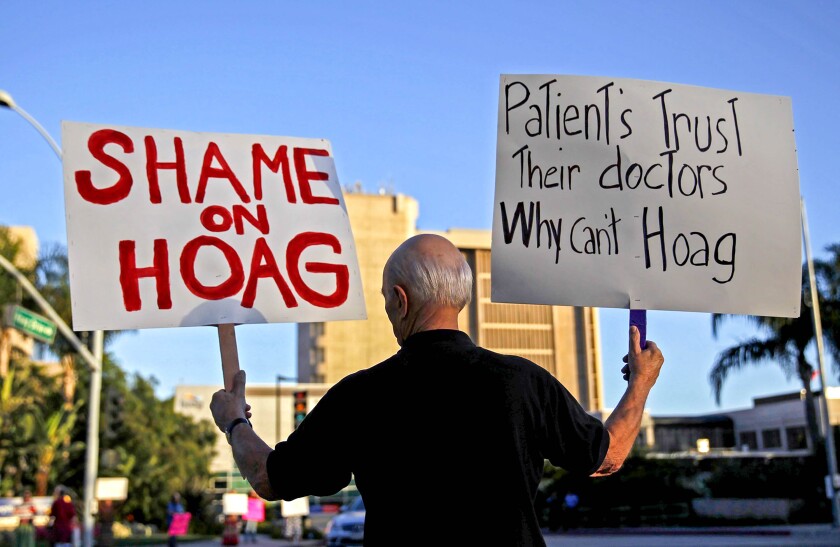 A protester holds one sign that says "Shame on Hoag" and another saying "Patients trust their doctors why can't Hoag."