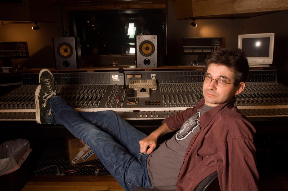 A man sits with his feet up on a mixing board in a recording studio