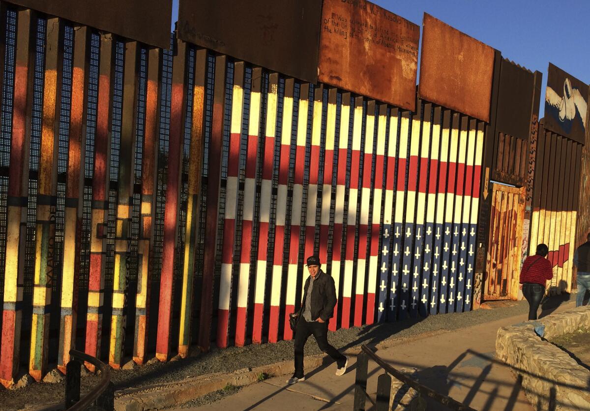 People walk past a mural of an upside down U.S. flag painted on the border fence