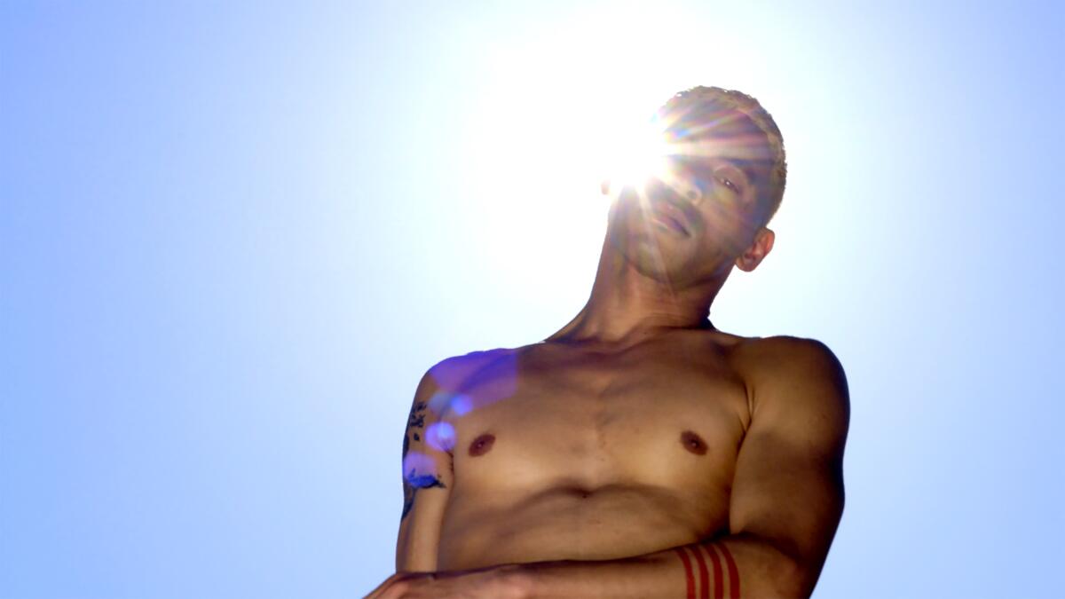 A shirtless man with the sun shining behind him.