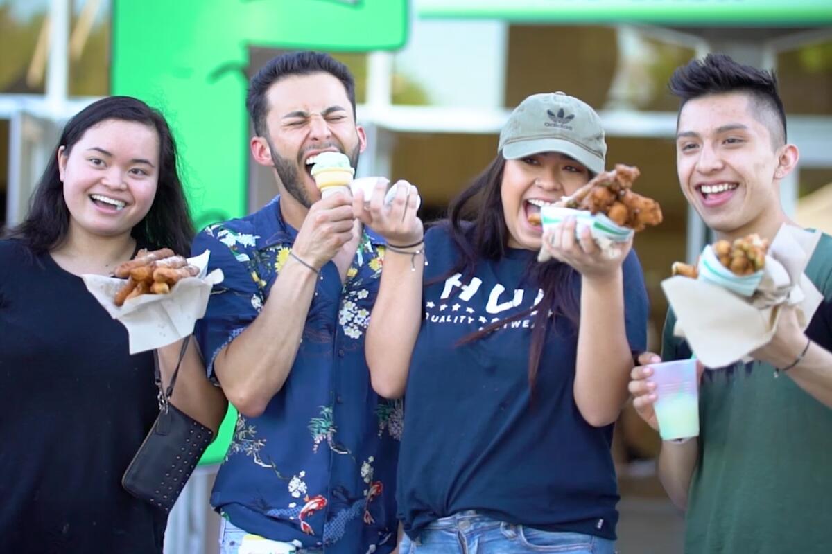 Four people stand outside eating paper-wrapped fair foods and smiling