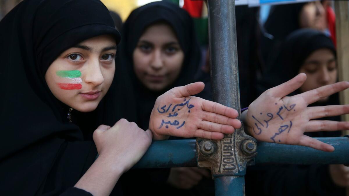 Two Iranian women, one with her face painted in the colors of the national flag, show their hands with writing in Persian that reads, "I'm ready to sacrifice myself for the Supreme Leader."