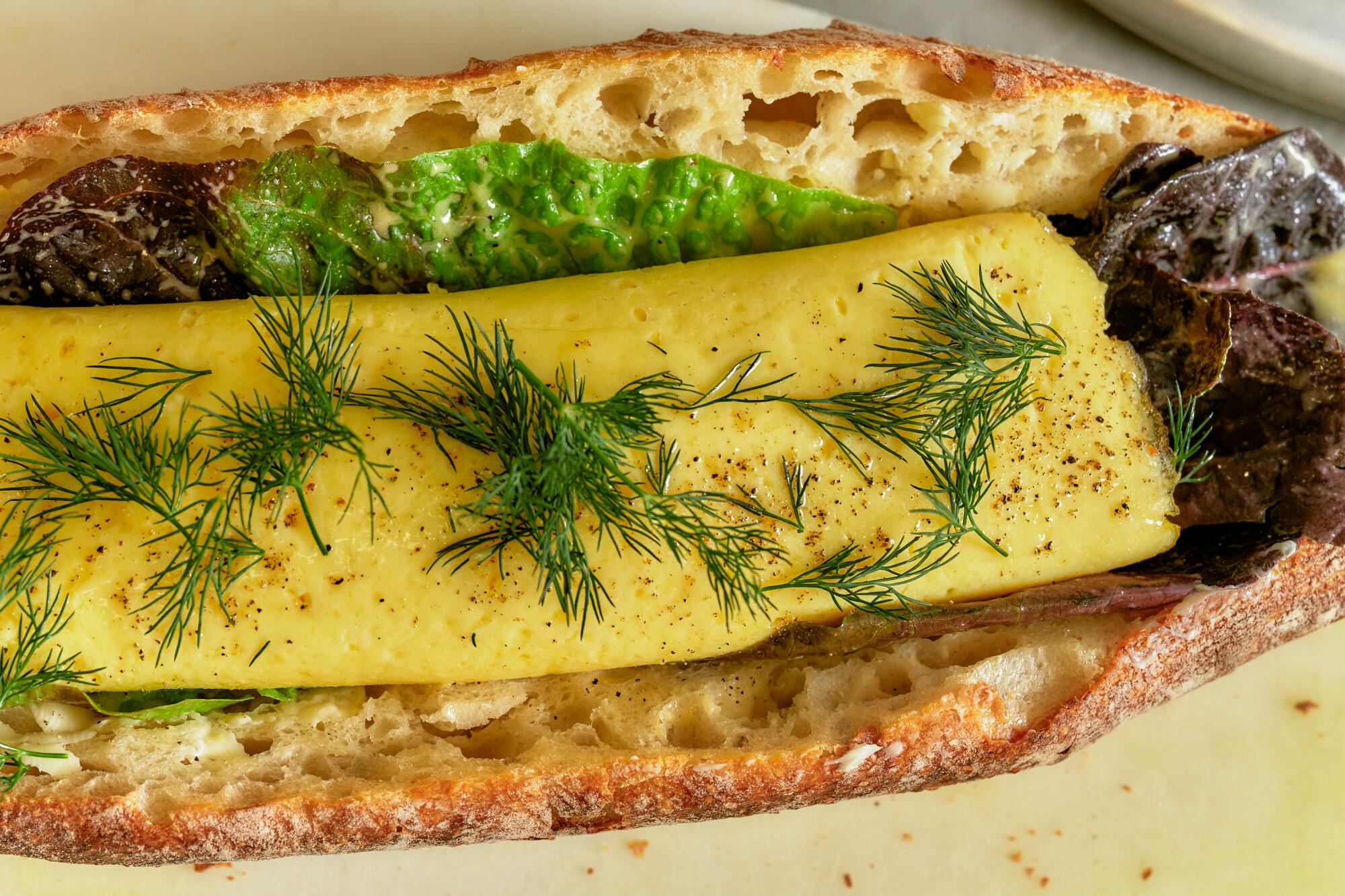 A split baguette holds an omelet sprinkled with dill