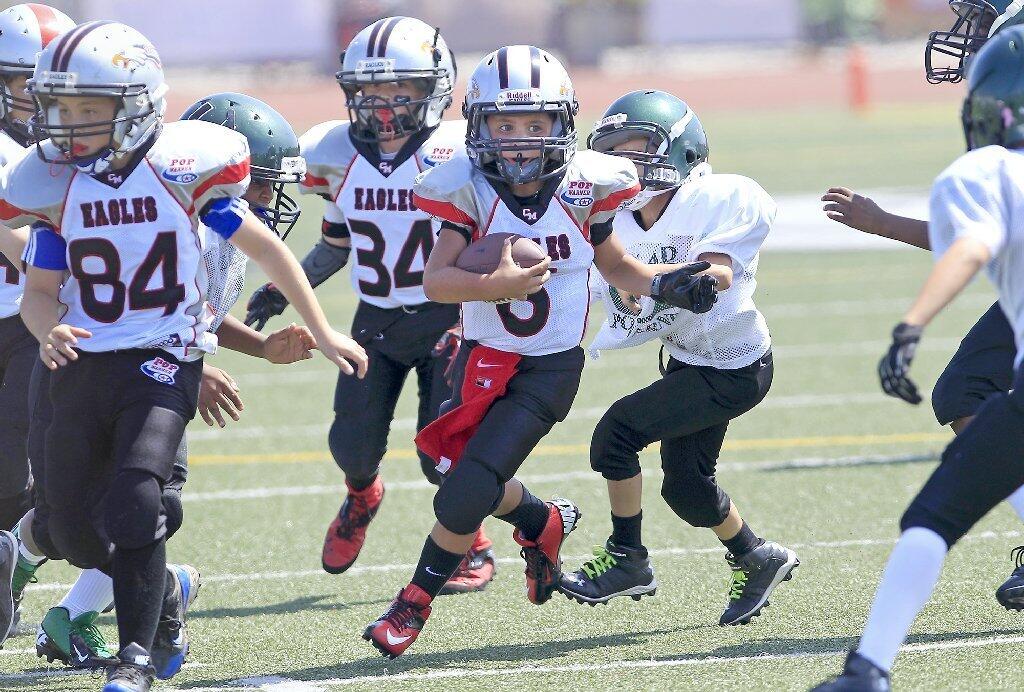 J.R. Mendez, center, carries the ball for the Costa Mesa Pop Warner Eagles of the Mighty Mites Division during a scrimmage against Upland at Jim Scott Stadium on Saturday.