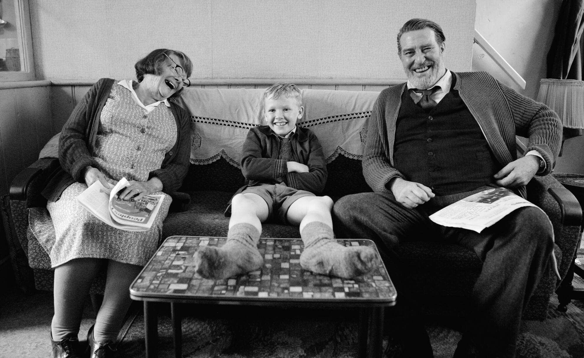 Judi Dench, Jude Hill and Ciarán Hinds have a laugh on the couch in a scene from “Belfast.”