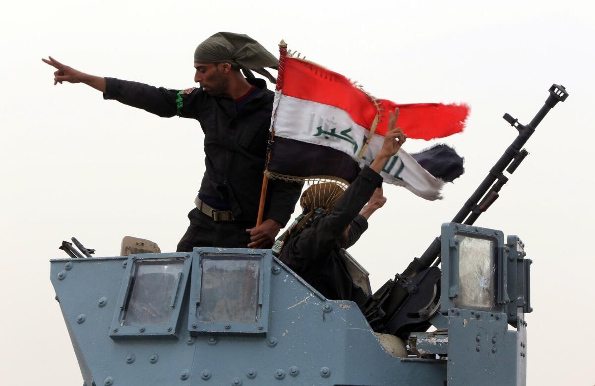 Iraqi troops wave the national flag Tuesday in celebration after securing a checkpoint from Sunni militants in the village of Badriyah outside the city of Mosul.