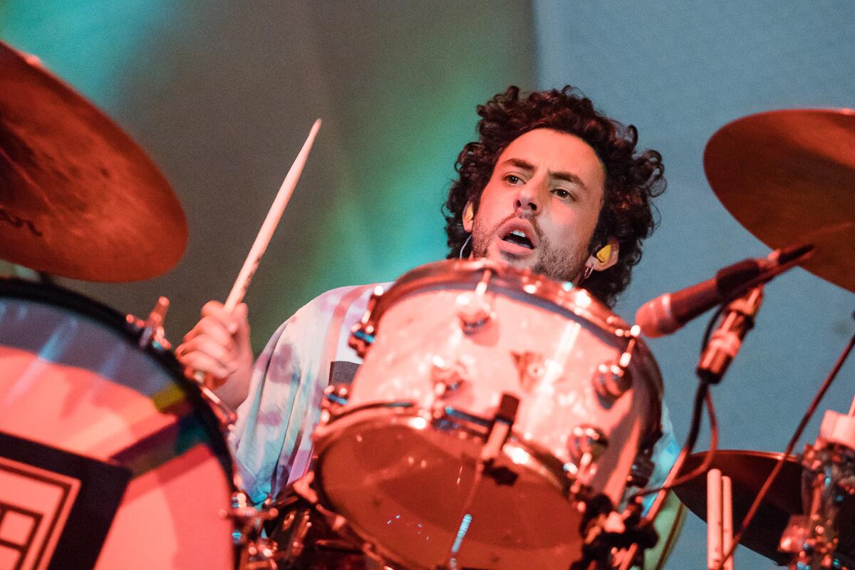 A dark-haired man holding drumsticks and sitting at a drum kit