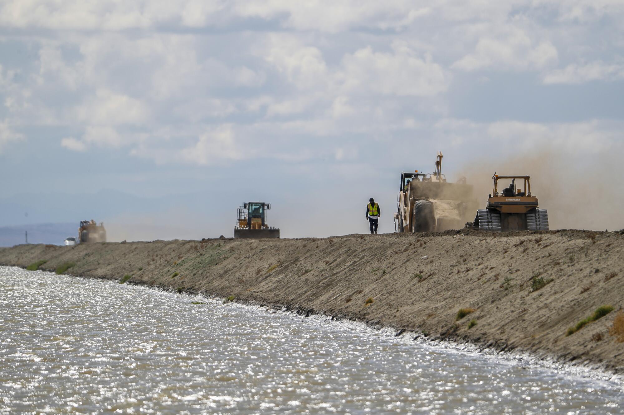 Crews use bulldozers to construct a levee to contain a swelling irrigation ditch.
