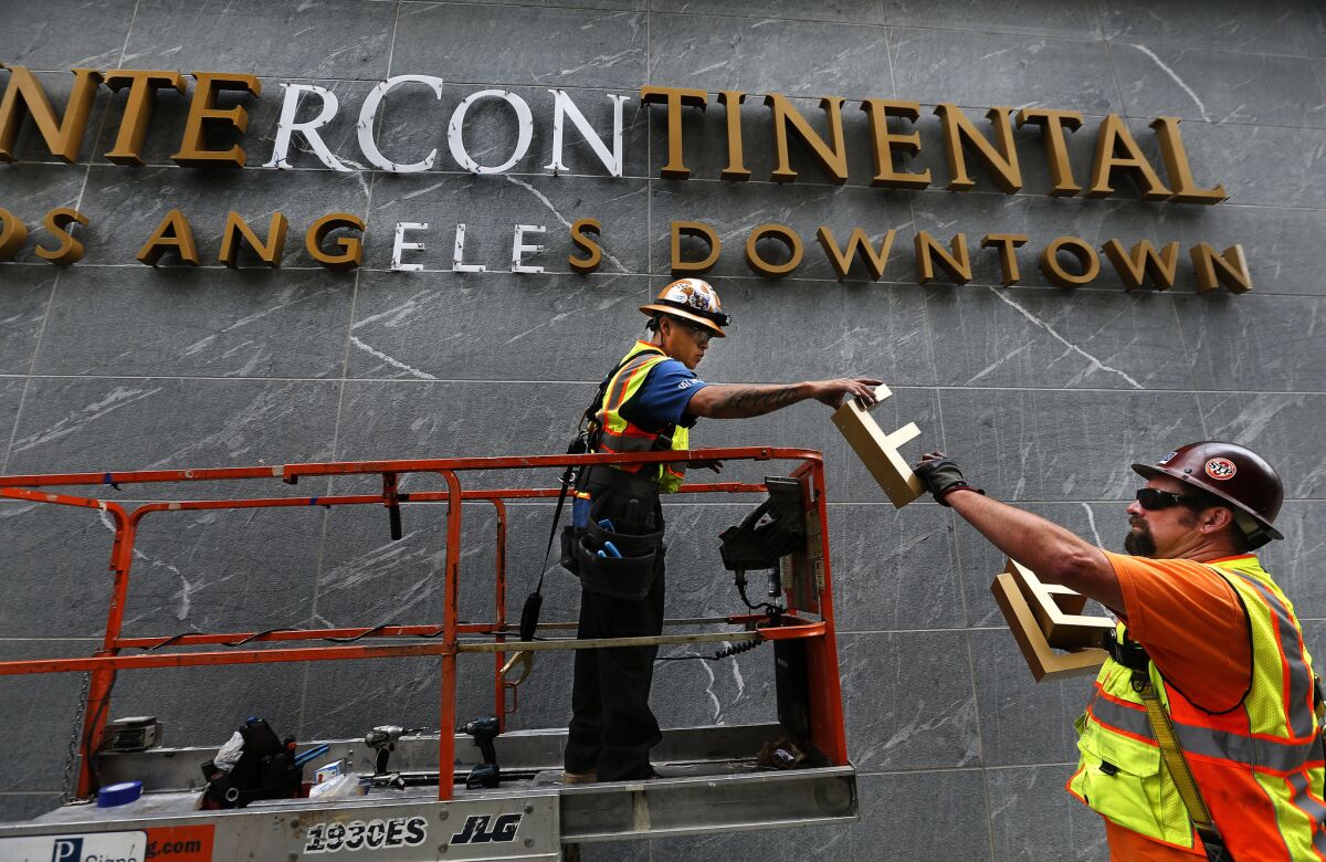 Workers install letters on an exterior wall..