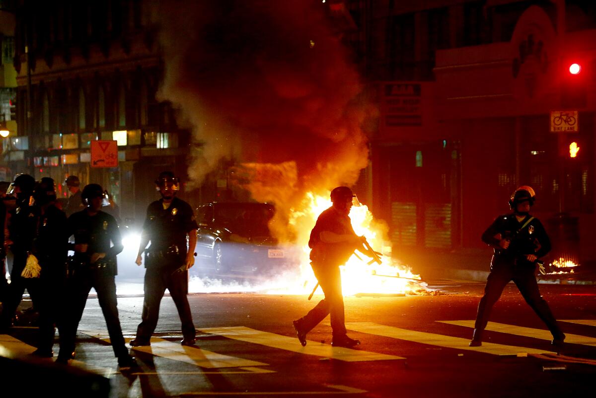 Police move past a fire set by protesters in downtown Los Angeles on Friday.