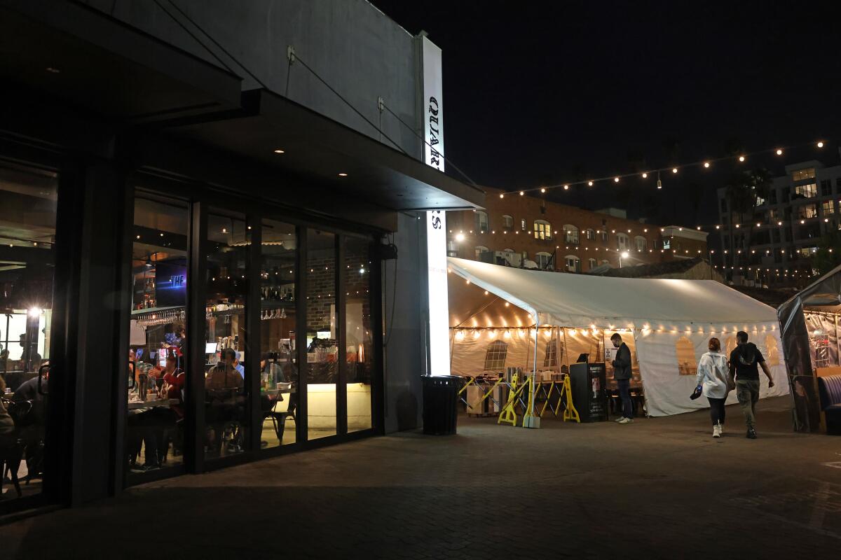 People walk past a packed restaurant with a dining tent outside