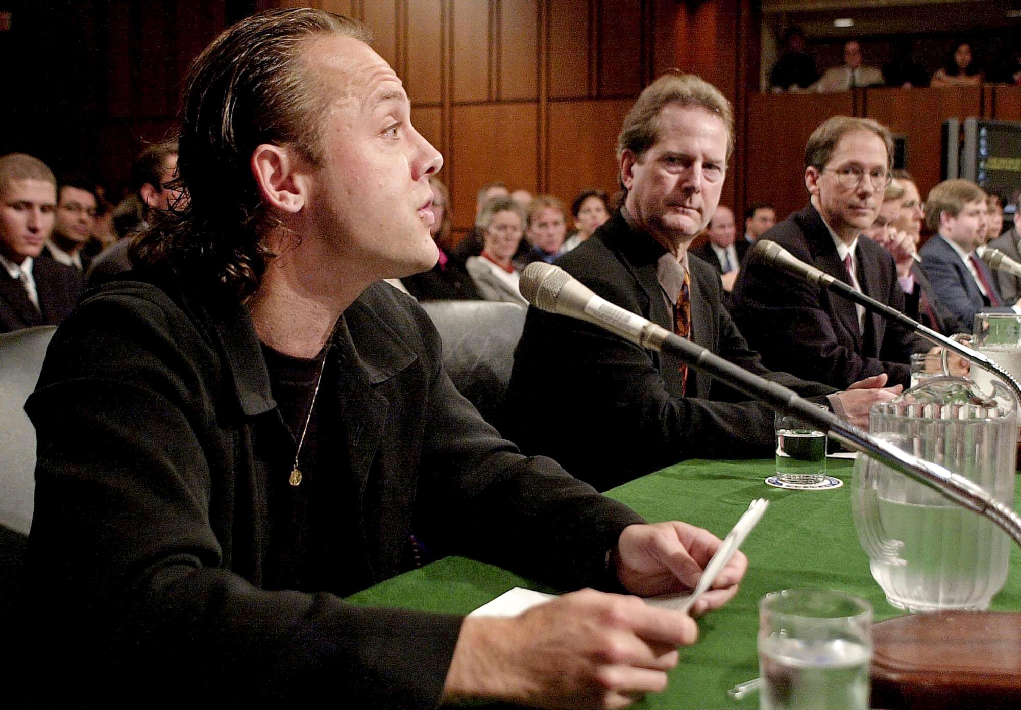 A man speaks into a microphone at a hearing as another man looks on.